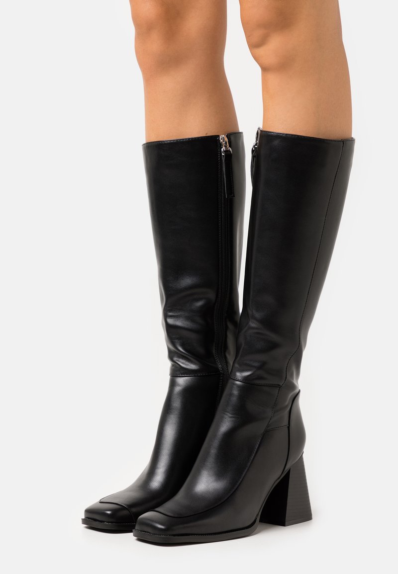 Botas de couro negras até ao joelho com bico quadrado e salto robusto. Apresentam um fecho lateral para fácil colocação e uma textura lisa e elegante.