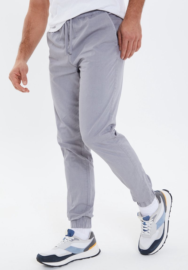 Helle graue Jogginghose aus Baumwolle mit elastischem Bund und Zugband, tapered Beinen und gerippten Bündchen. Kombiniert mit sportlichen Sneakers.
