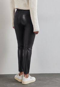 Svarta byxor i fejkläder med en smal passform, hög midja och två bakfickor, kombinerade med vita sneakers och en mysig krämfärgad tröja.