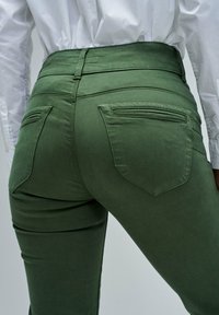 Olivno zeleni hlače, prilegajoče se, z gladko teksturo, visokim pasom in dvema zadnjima žepoma s sleek dizajnom.