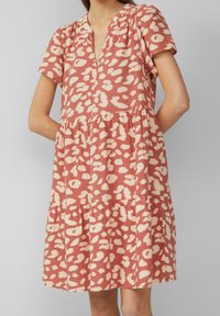 Donna che indossa un vestito corto, maniche corte, scollatura a V e lunghezza fino al ginocchio, con un motivo animalier in rosa polveroso e crema.