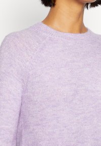 Lilat neulosneulepaita pyöreällä pääntiellä, pehmeällä tekstuurilla ja raglan-hihoilla, joissa on hienovaraisia värivaihteluita kauttaaltaan.