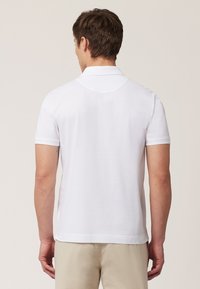 Witte polo met korte mouwen, klassieke kraag, platte brei textuur en zijsplitten aan de onderkant. Achteraanzicht toont een glad, gelijkmatig stof.