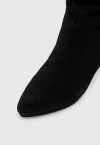 Botte cheville en suede noir avec un bout pointu et une tige ajustée. La surface est lisse et sans quincaillerie ni accents visibles.