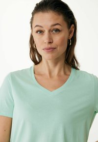 Mátově zelené tričko s výstřihem do V vyrobené z měkké tkaniny s krátkým rukávem. Charakterizuje ho hladká textura a jednoduchý design bez vzorů či akcentů.