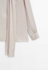 Blouse rose clair en tissu doux, dotée de manches longues et d'un détail de foulard drapé. L'ourlet est droit, sans motifs ni accents.