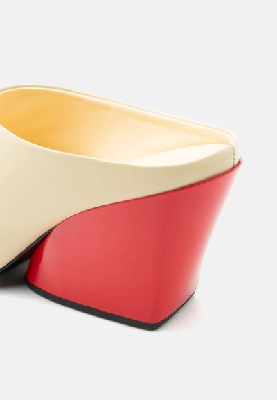 Δερμάτινο mule σε κρεμ απόχρωση με πλατιά, ψηλή σφήνα σε γυαλιστερό κόκκινο και μαύρη σόλα, εμφανιζόμενο από πίσω γωνία.