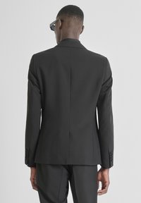 Zwarte getailleerde blazer met gestructureerde schouders, enkele achterventilatie en gladde stof. Heeft een strak, gestroomlijnd ontwerp zonder versieringen.