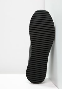 Svart sneaker-sula med djupa, horisontella spår. Materialet verkar vara gummi med en texturerad yta. Något avsmalnande mot baksidan.