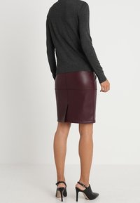 Suéter de carbón con una falda ajustada de cuero sintético burdeos que presenta una abertura trasera, combinado con zapatos de tacón negro.