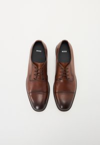 Scarpe eleganti in pelle marrone con una finitura liscia, design a punta centrale e chiusura con lacci. Presentano un logo discreto sulle sole. 