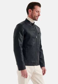 Zwarte faux leren jas met een staande kraag, voorrits, zijzakken en gequiltte schouderaccenten. Heeft een soepele textuur.