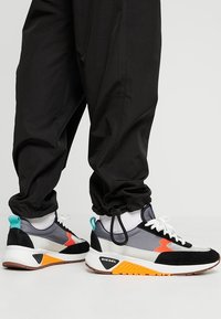 Black and gray athletic sneakers with orange and teal accents, featuring a mix of suede and mesh materials and a textured rubber sole.