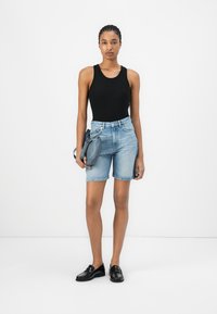 Top negro sin mangas, pantalones cortos de mezclilla azul claro, mocasines negros y una bolsa gris. Diseño simple, forma ajustada y detalles de herrajes mínimos.