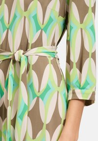 Chiffonkleid mit einem mehrfarbigen geometrischen Muster in Grün, Mint und Beige, mit einem Bindegürtel und Dreiviertelärmeln.