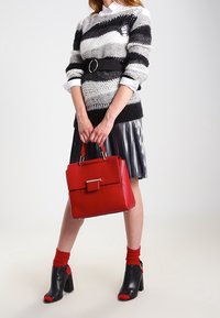 Sac à main structuré rouge avec une finition texturée, associé à un pull rayé noir et blanc, une jupe plissée et des bottines noires à talons.