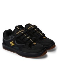 Black athletic shoes featuring a mesh and synthetic upper, thick black sole, gold accents, and elastic laces for secure fit.