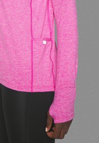 Vartaloa myötäilevä pitkähihainen paita kirkkaanpinkissä, valmistettu teksturoidusta kankaasta. Sisältää peukaloreiät ja kontrastiväriset tikkaukset sivuilla.