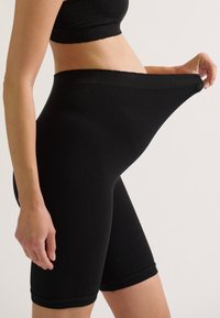Zwarte geribbelde shorts met een hoge taille en rekbare stof, die een elastische textuur en een strakke pasvorm rond de dijen laten zien.