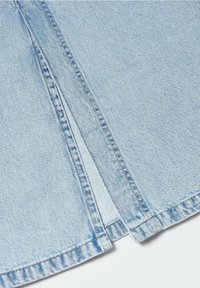 Gros plan sur un tissu denim bleu clair avec des coutures doubles visibles et une petite fente au bas.