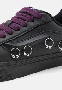Svarte lær sneakers med lilla snøring og sølvringer langs siden nær sålen.