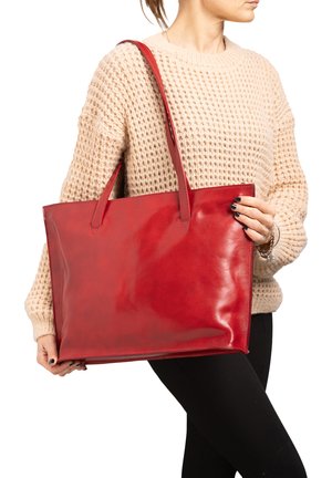 Borsa a tracolla rossa in pelle con due manici, forma rettangolare, texture liscia e senza hardware visibile. Maglione di cotone indossato da una modella.