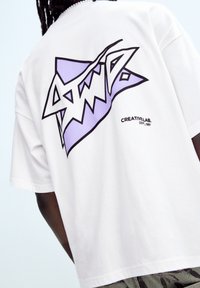 T-shirt in cotone bianco con una grande grafica viola e nera sul retro caratterizzata da un design frastagliato, con il testo "CREATIVLAB. DEPT. 1991" sottostante.