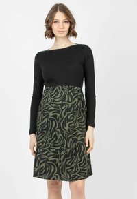Schwarzes Rippenoberteil mit langen Ärmeln, das in einen Rock mit grünem und schwarzem abstraktem Muster übergeht, schafft eine taillierte Silhouette und A-Linienform.