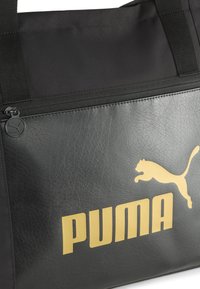 Zwarte synthetische tas met een gestructureerde afwerking, gouden logo-ontwerp en een ritsvak. Versterkte banden voor duurzaamheid.