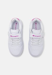 Baskets blanches avec un design élégant, présentant un bout perforé, des lacets en tissu et une sangle Velcro. Accents de logo rose sur les côtés.