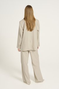 Beige op maat gemaakt pak met een losse pasvorm, met een enkelgeknoopte blazer met knopen en wijde broekspijpen, gemaakt van een zachte stof.