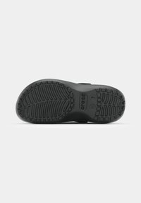 Semelle de chaussure Crocs noire avec motif texturé, taille W7, affichant le nom de la marque et le site web sur fond blanc.
