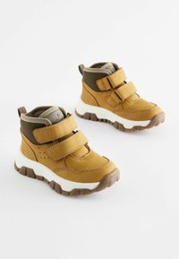 Tan- och bruna anklarboots med två justerbara kardborreband, en vadderad krage och en strukturerad gummisula för bättre grepp.