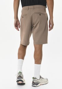Beige shorts met een getailleerde pasvorm, twee achterzakken met knopen, gecombineerd met grijze hardloopschoenen en witte enkelsokken.