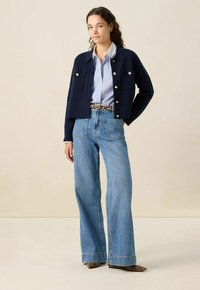 Marine gebreide cardigan met gouden knopen over een blauw-wit gestreept shirt, gecombineerd met hoge taille wijdvallende denim jeans.