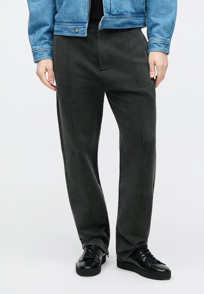 Pantalones de algodón gris oscuro con corte recto, con costuras frontales y laterales, combinados con zapatillas negras. La tela tiene una textura suave.