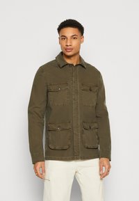 Chaqueta verde oliva con un cierre de botones en el frente, dos bolsillos en el pecho y un cuello. Confeccionada con un tejido duradero y un diseño informal.