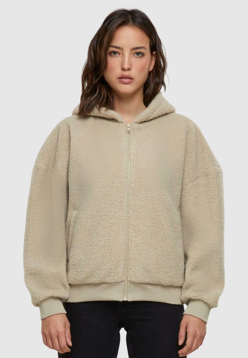 Giacca beige con cappuccio e zip realizzata in morbido fleece testurizzato, con maniche oversize, polsini a coste e due tasche laterali.