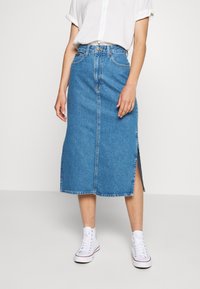 Vaaleansinisestä denimmidihameesta, jossa on suora leikkaus, sivuhalkio ja repsottavat reunat. Yhdistetty valkoisiin korkean nauhan tennareihin.