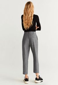 Grijze geruite broek met een getailleerde pasvorm, voorzien van zijzakken en een omgeslagen zoom. Draagt daarbij een zwart top met lange mouwen en zwarte sneakers.