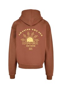 Felpa con cappuccio marrone con stampa grafica gialla sul retro, che presenta un design di sole e onde, e il testo: "Inseguendo il Sole", "Just Rhyse", "EST. 2015."