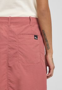 Shorts rose avec une poche arrière. Fabriqués en tissu léger. Dotés d'une ceinture cousue et d'une petite étiquette de marque sur la poche.