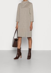 Robe en tartan beige avec un col bénitier, manches trois-quarts ; associée à des bottines marron embossées croco et un sac à main assorti.