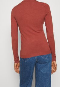Langdurige mouwen, roestkleurige trui gemaakt van zacht breiwerk. Slanke pasvorm met geribbelde boorden en zoom. Draag met blauwe high-waisted jeans.