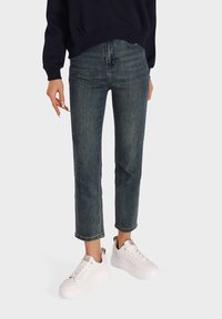 Jeans in denim blu scuro con taglio dritto, dotati di vita intermedia e leggero sbiadimento, abbinati a sneakers bianche con soletta a piattaforma.