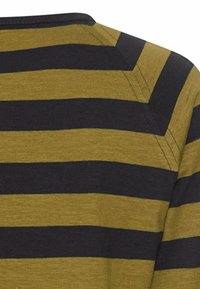 Nahaufnahme von Stoff mit abwechselnd breiten horizontalen schwarzen und olivgrünen Streifen sowie sichtbaren Nahtstichen an der Schulter eines Kleidungsstücks.