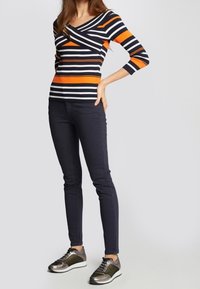 Maglietta a maniche lunghe a righe con strisce alternate in blu navy, arancione e bianco; abbinata a jeans scuri slim-fit e sneaker metallizzate.