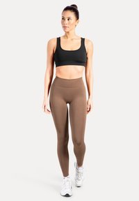 Schwarzer Sport-BH kombiniert mit hoch taillierten, braunen Leggings. Die Leggings sind eng anliegend mit einer glatten Textur und eignen sich für sportliche Aktivitäten.