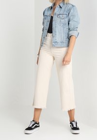 Světlě modrá džínová bunda s ohrnutými rukávy, černý top, bílé zkrácené kalhoty s roztřepeným lemem a černobílé tenisky.