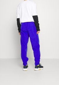 Blå fleecebyxor med elastisk midja, med en avslappnad passform. Matchas med en vit och svart långärmad tröja och sneakers.